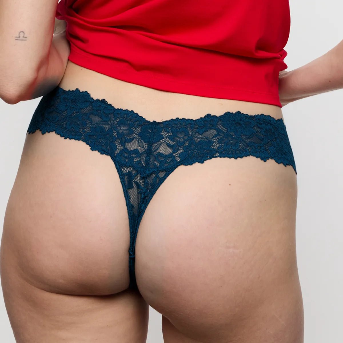 Person i Marie Jo Soft-sæt i mørkeblå, rød top og blå g-streng med blonde-detaljer, set bagfra.