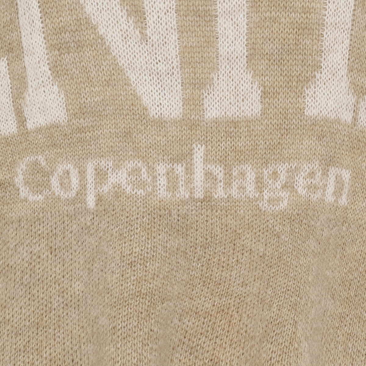 Nærbillede af beige strikstof, Marta du Château Aria Sand, hvor ordene »Copenhagen« og hvide bogstaver kan ses.