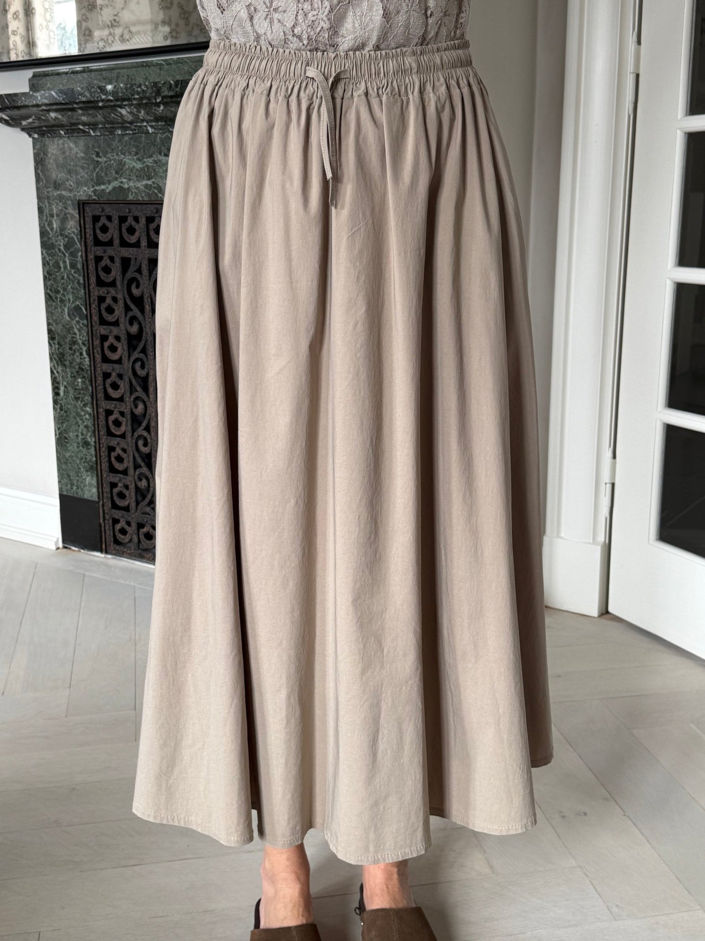 En person iført en Marta du Château – Pomeline Sand-nederdel med elastisk linning, der står indendørs på et lyst gulv.