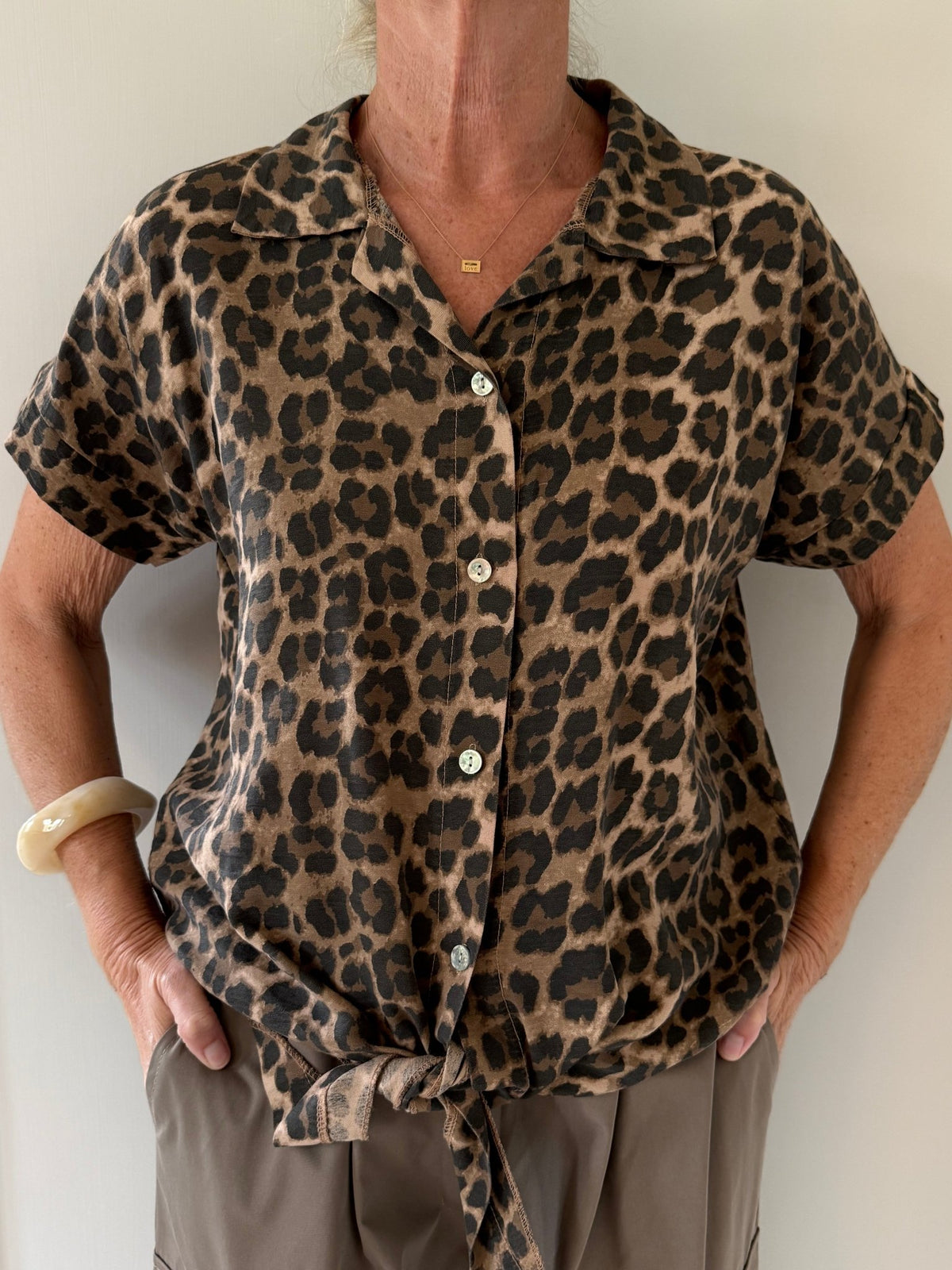 Model iført en Marta du Château Vianne-top med leopardmønster, korte ærmer, bånd foran og hænderne i lommerne.
