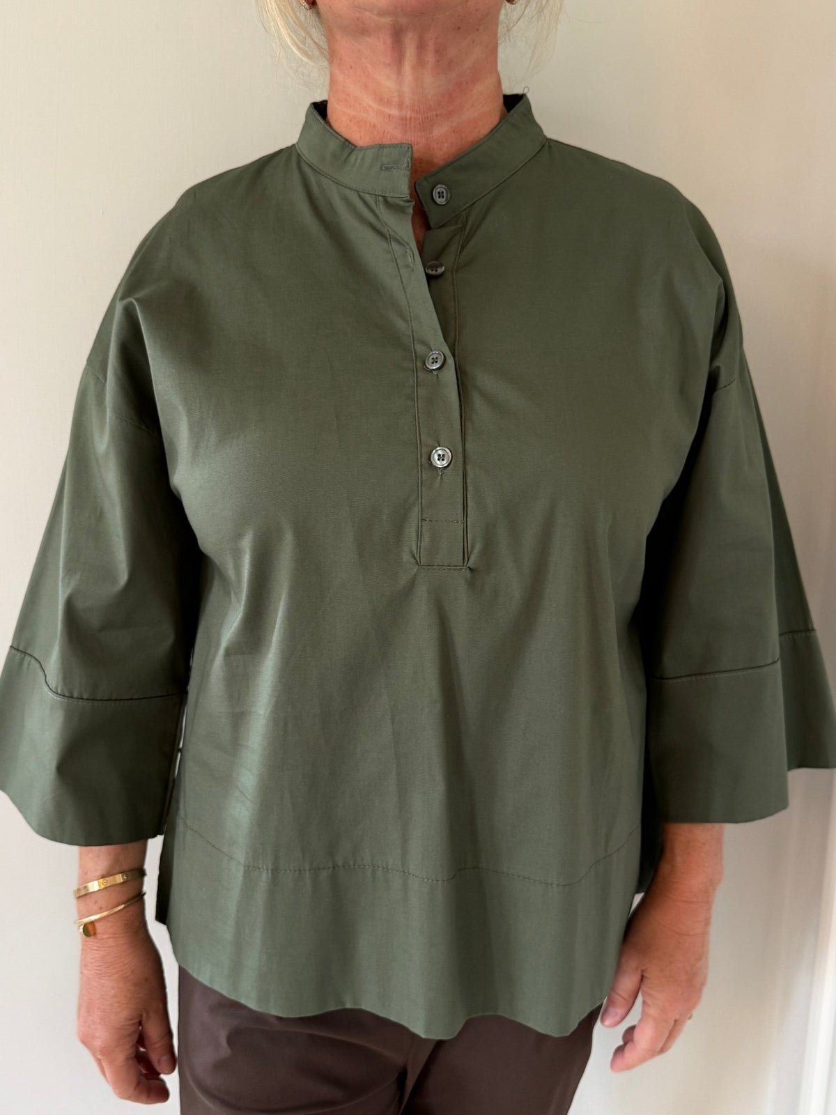 En person iført den grønne Marta du Château Ginger Army-bluse med brede ærmer, fotograferet foran en ensfarvet lys væg.