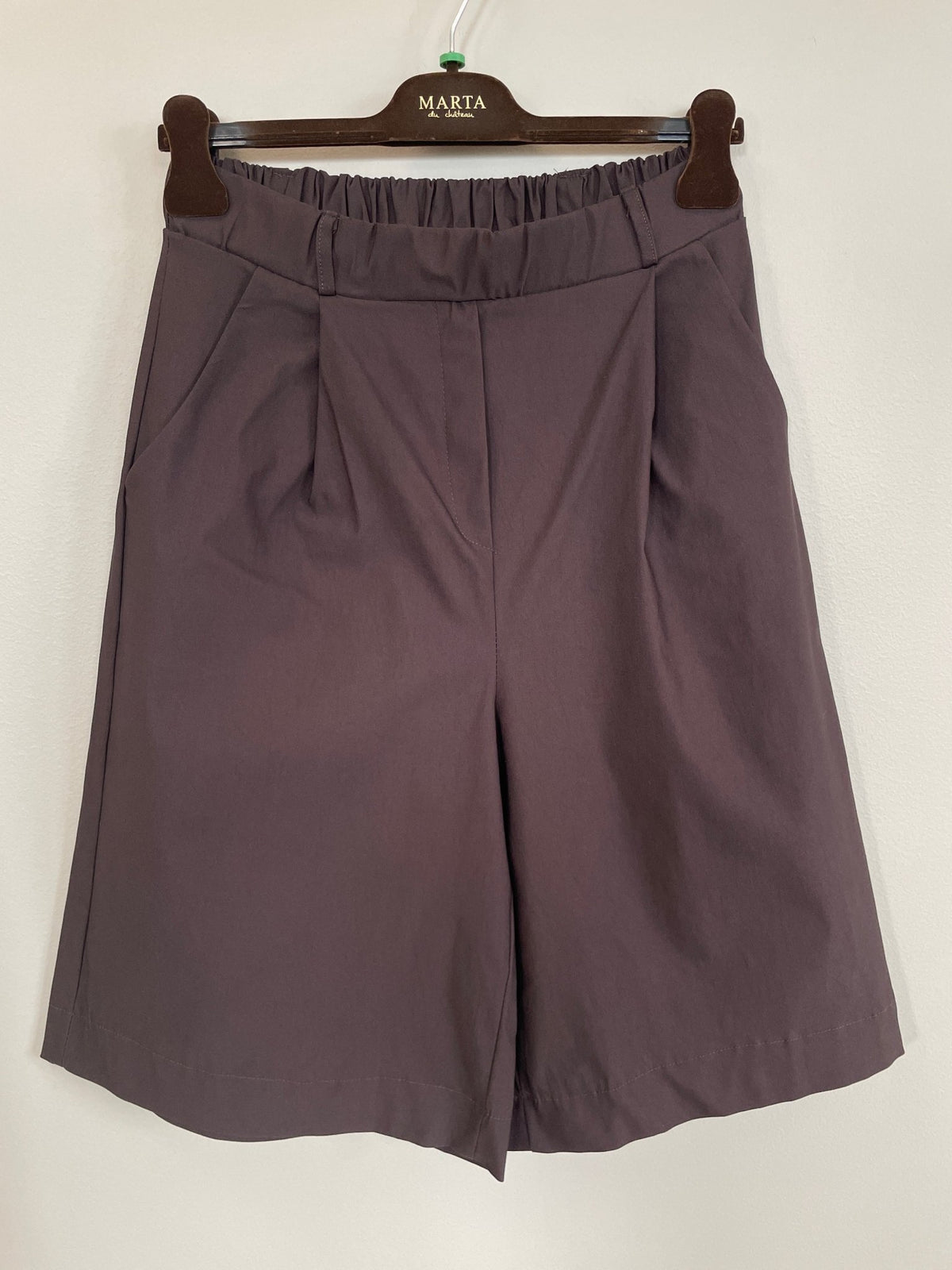 Marta du Château 156162 MDCBrunella: brune shorts med høj talje og plissering, der går til knæet, vist på en bøjle ved en lys væg.