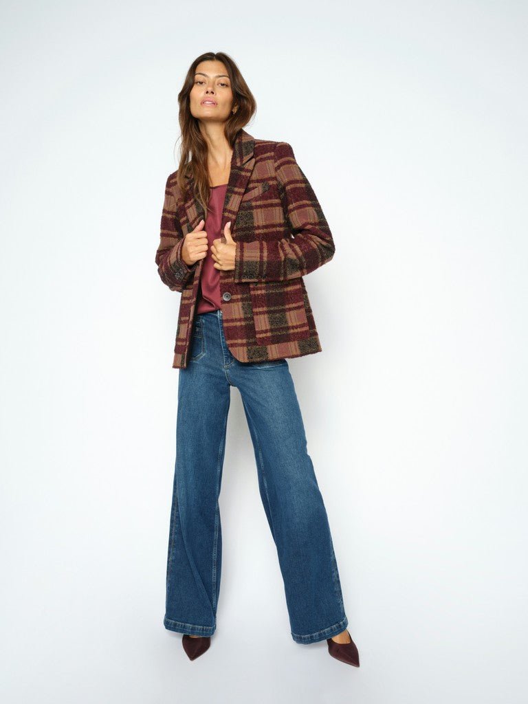 En kvinde i en ternet blazer, en rødbrun bluse og MOS MOSH Colette Denim-jeans står foran en ensfarvet hvid baggrund.