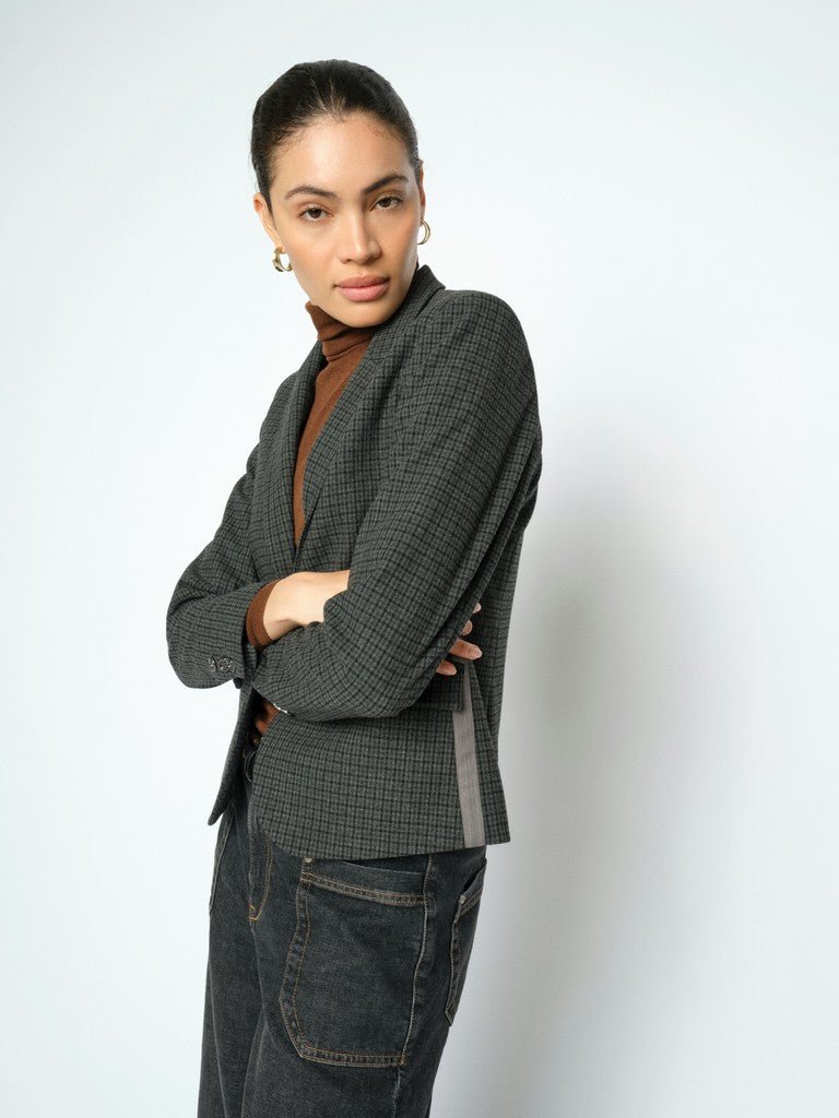 En kvinde iført en MOS MOSH Josa Ternet-blazer i ternet mønster, en brun rullekravebluse og mørke jeans står foran en hvid baggrund.