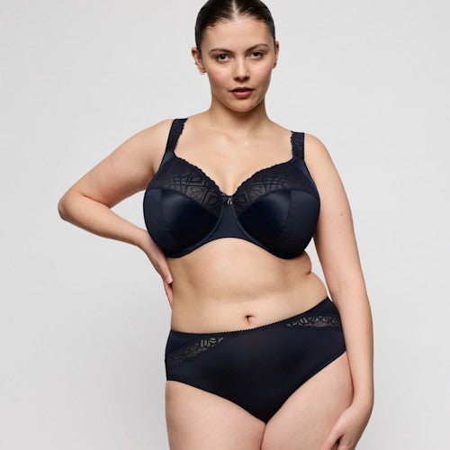 En kvinde har PrimaDonna Salerno-maxi-trusser og -bh i farven Midnight Blue på og poserer foran en ensfarvet lys baggrund.