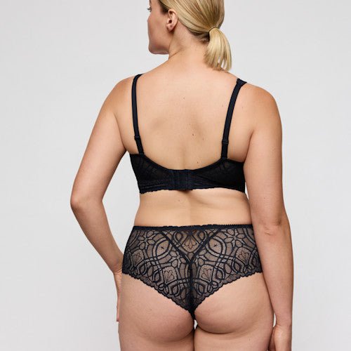 En kvinde i elegant blonderundertøj har en PrimaDonna Salerno Midnight Blue G-streng på; hun står med ryggen til kameraet foran en ensfarvet baggrund.