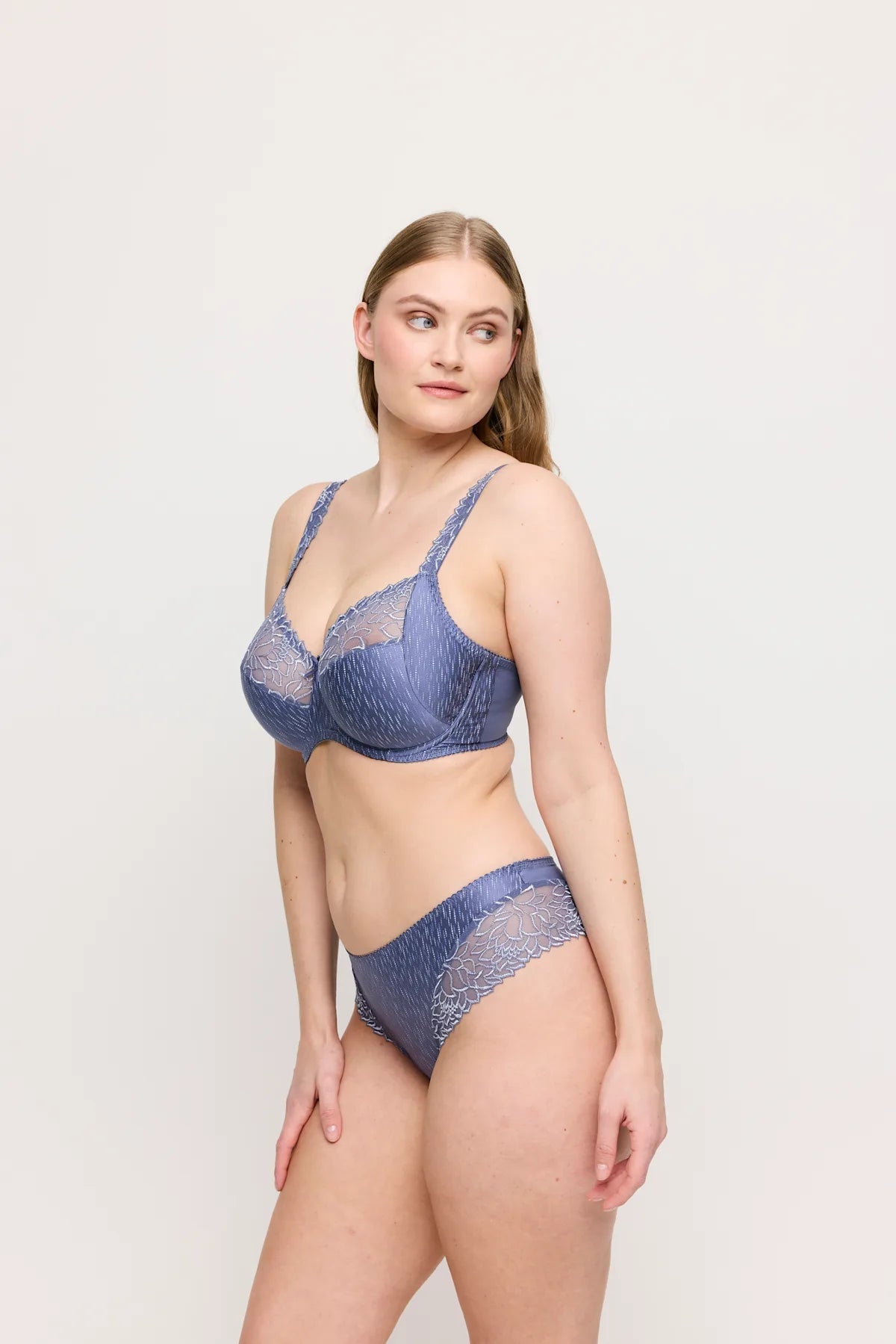 Modellen bærer en PrimaDonna Monterrey Nightshadow Blue Blå bh med fulde skåle og trusser, står med hånden langs siden og kigger mod venstre.