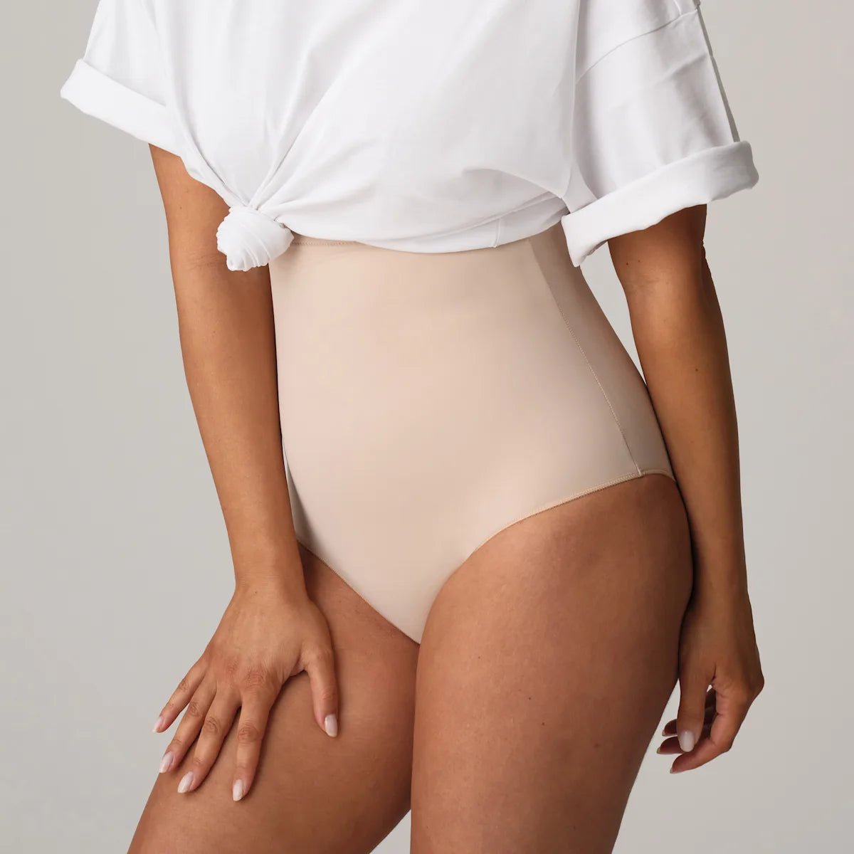 En selvsikker kvinde i en hvid T-shirt og PrimaDonna 155145 Perle Caffe Latte Pudder-figurformende undertøj, der giver en glat silhuet.