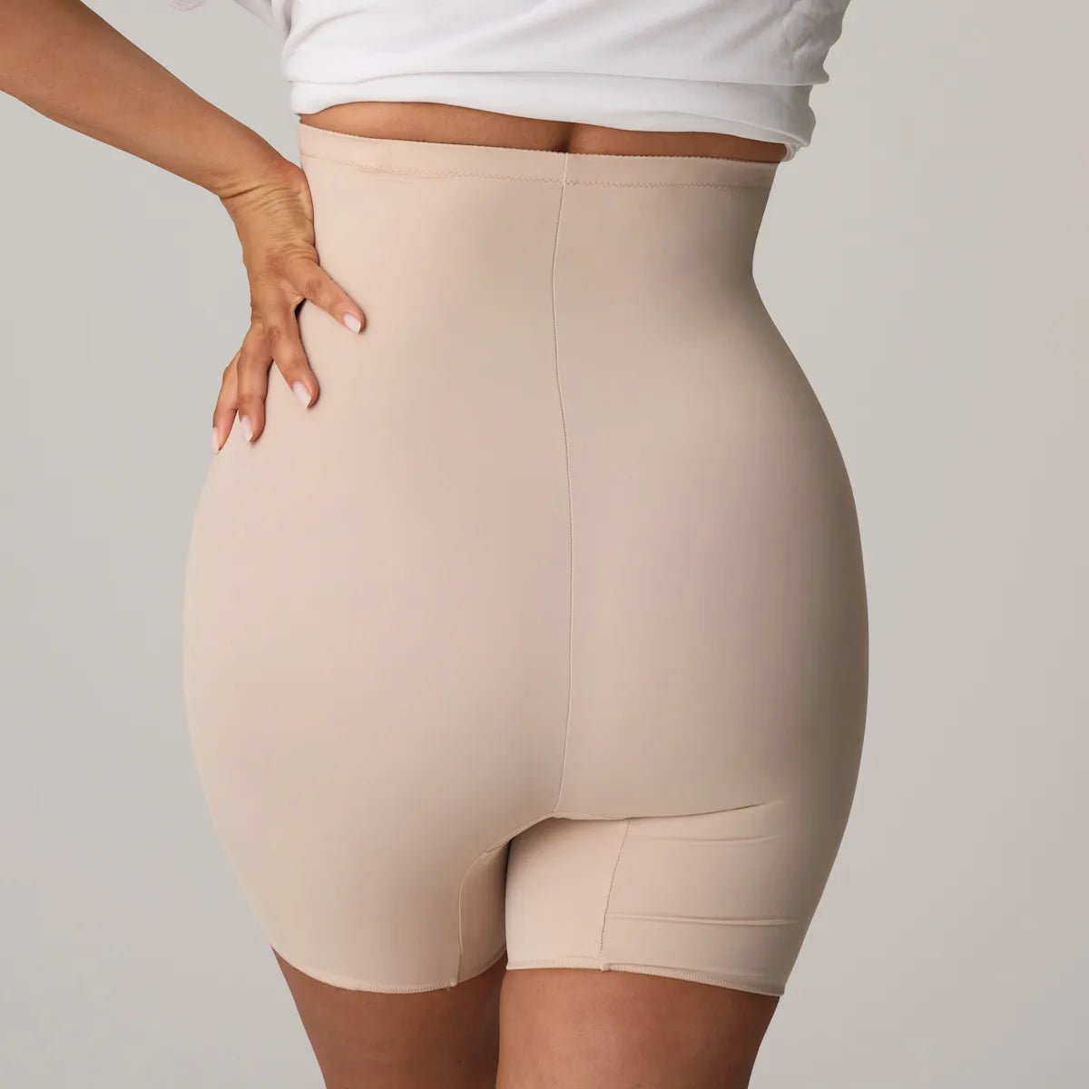 En person iført PrimaDonna Perle Caffe Latte Pudder-figurformende undertøj og en hvid crop top, set bagfra.