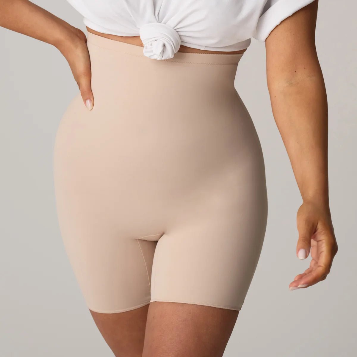 En person iført en hvid skjorte med knapper og PrimaDonna Perle Caffe Latte Pudder-figurformende undertøj, der står foran en ensfarvet baggrund.