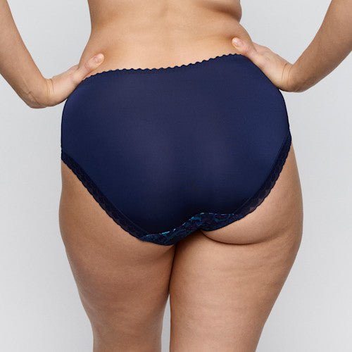 Feminine detaljer fremhæver PrimaDonna San Angel Water Blue-trusset, der ses set bagfra med hænderne på hofterne foran en neutral baggrund.
