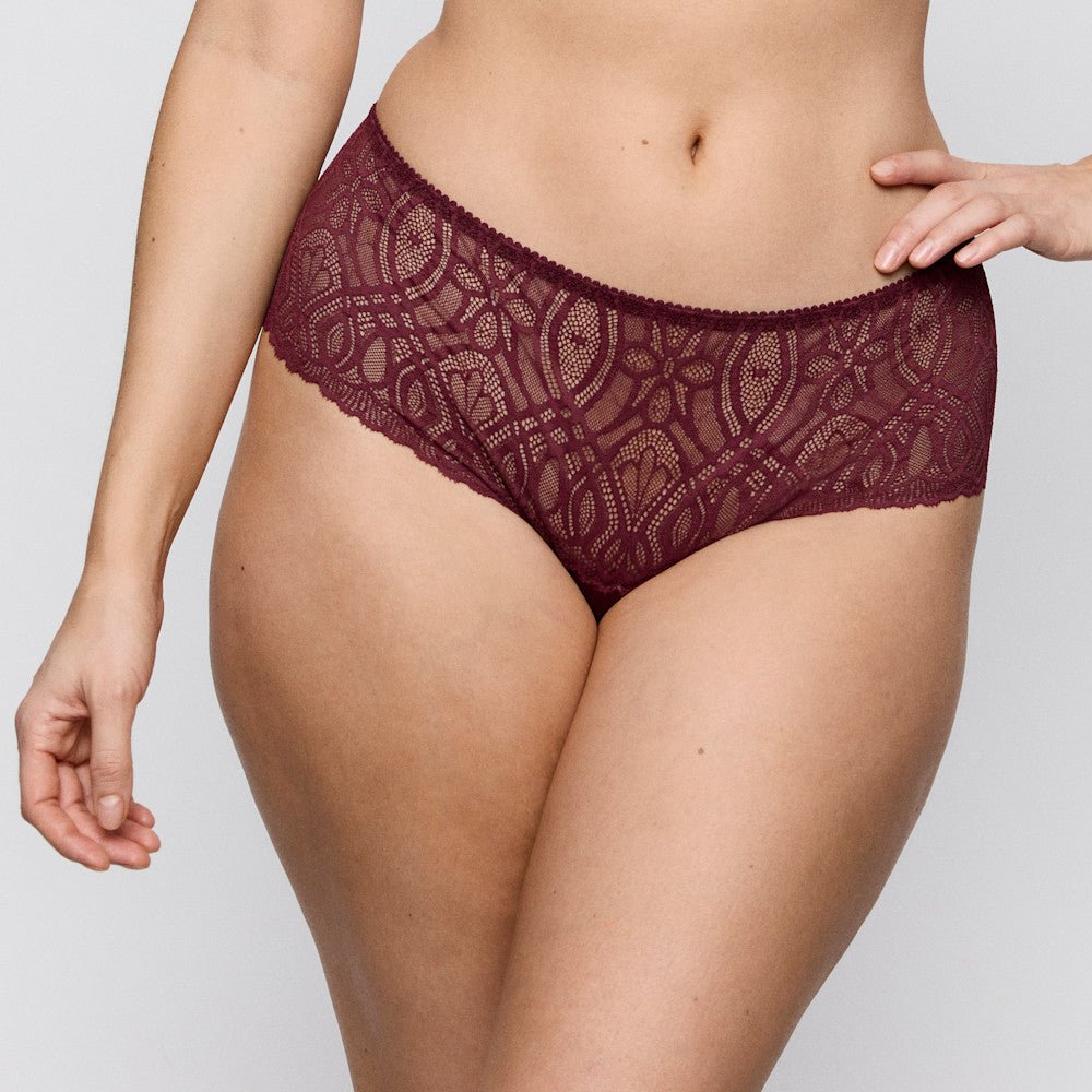 En person har PrimaDonna 155417 G-streng i farven Evening Red Bordeaux på, vist fra midten af overkroppen til lårene foran en ensfarvet baggrund.