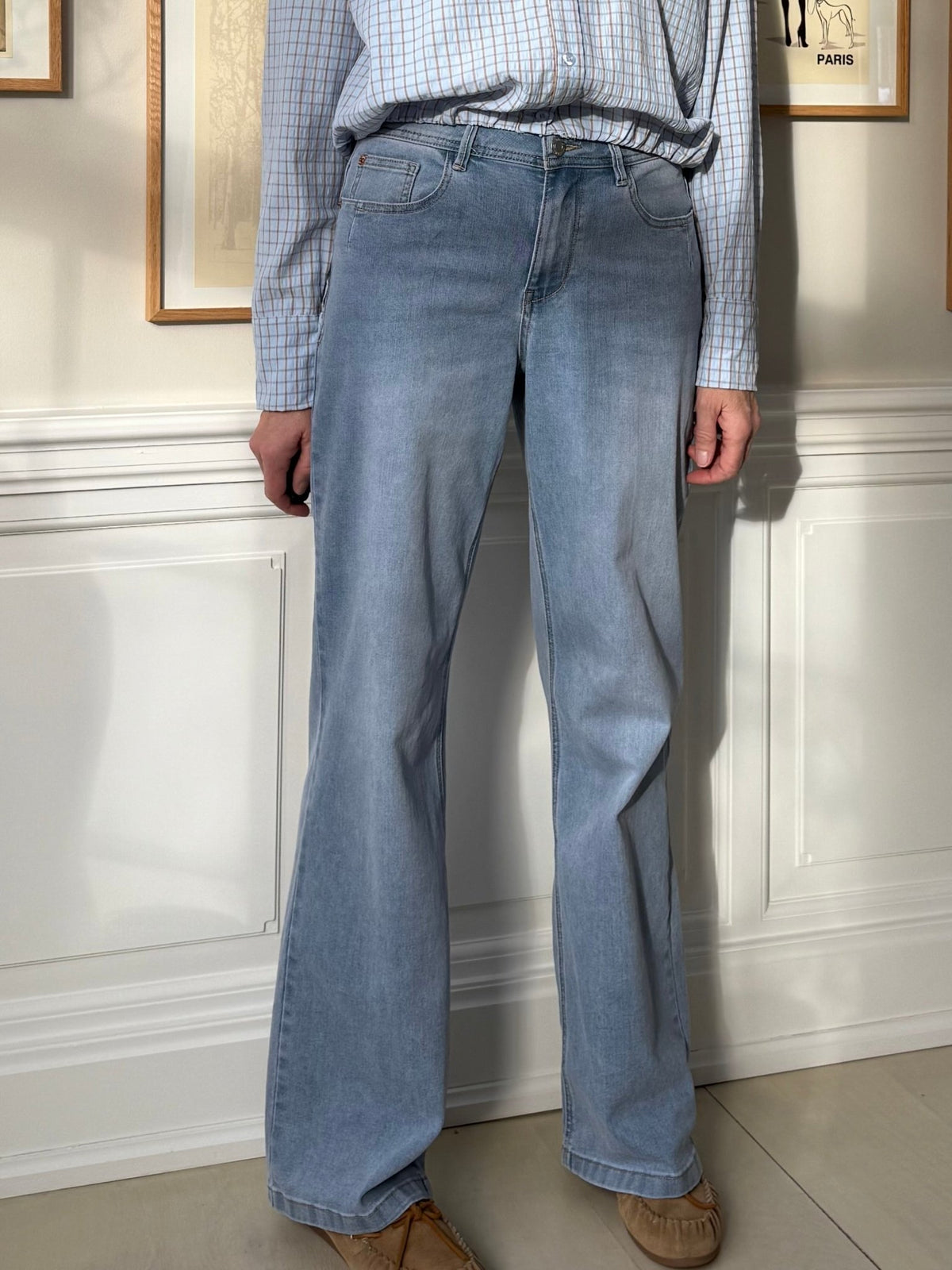 En person iført Red Button Colette L33 Lys-jeans og en ternet skjorte, der står indendørs ved en hvid væg.