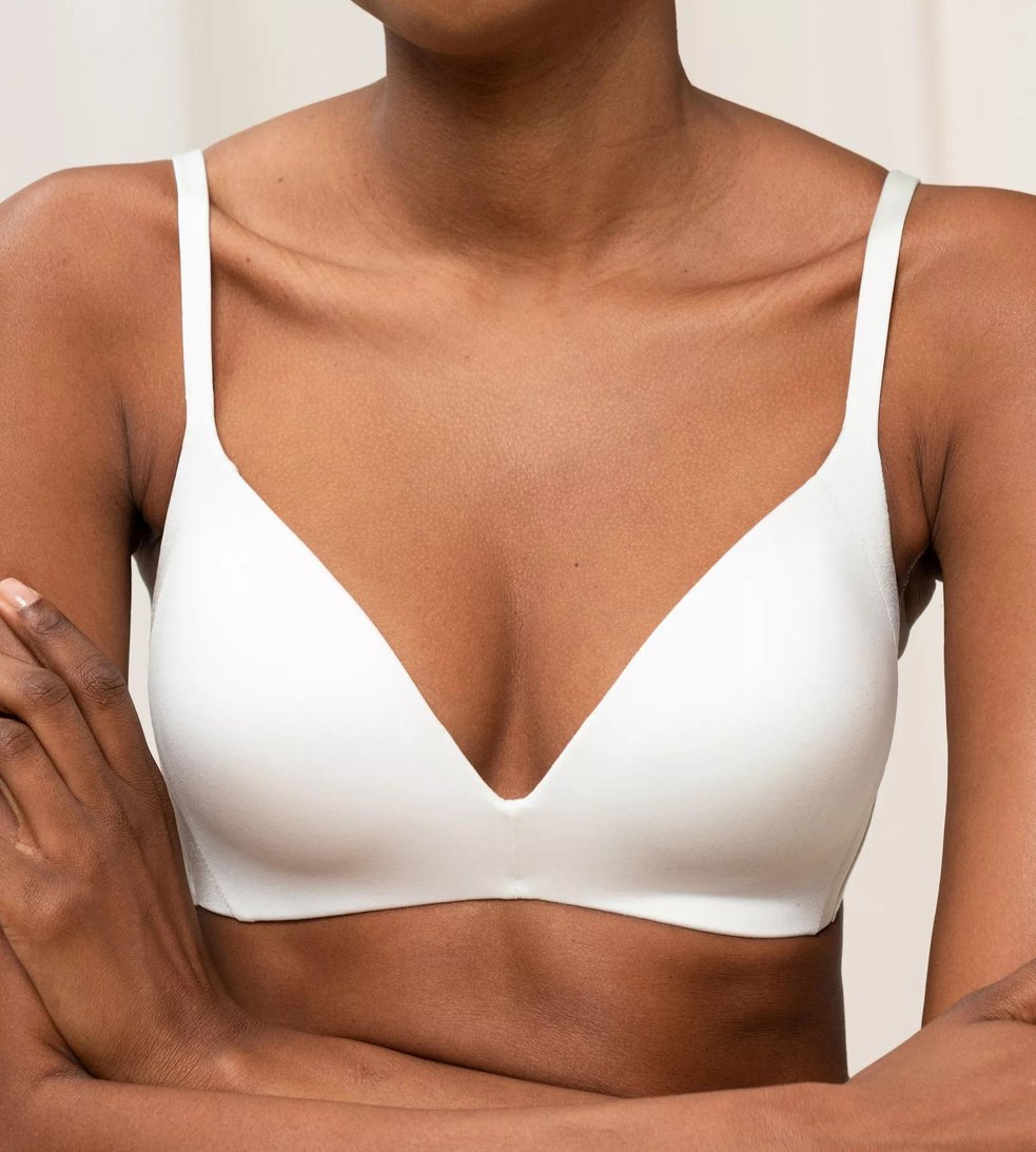 Model iført Triumph 149083 Body Make-up Soft Touch Off White, med armene over kors, foran en neutral baggrund.