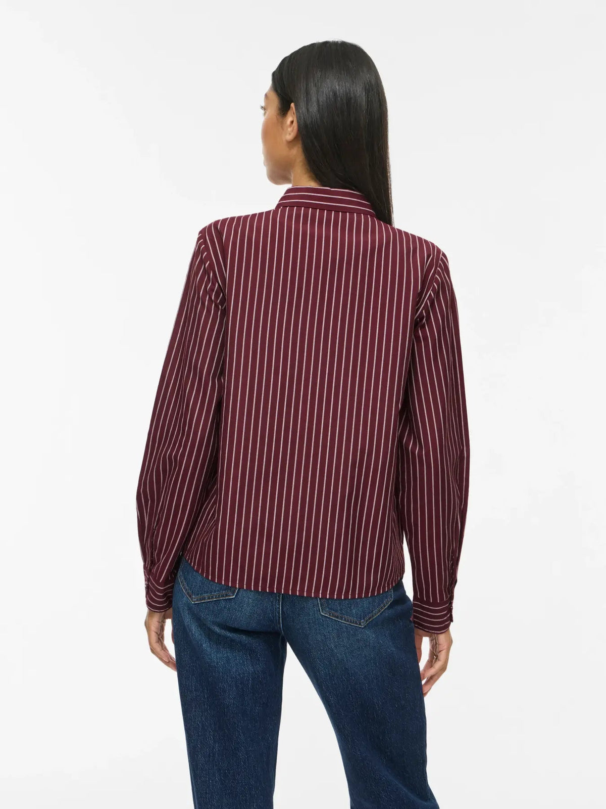 En person iført en VILA Vidarma Bordeaux-skjorte og blå jeans, set bagfra foran en ensfarvet baggrund.