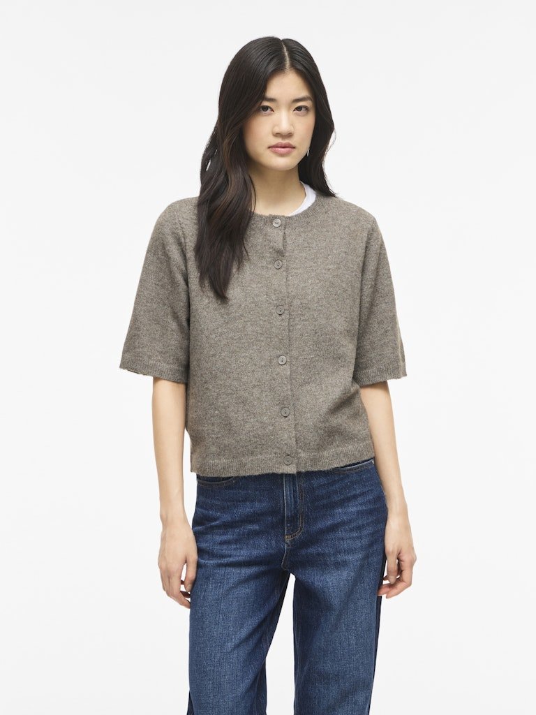En kvinde har en kortærmet 155226 VILA – Viliga gråmeleret cardigan og blå jeans på foran en hvid baggrund.