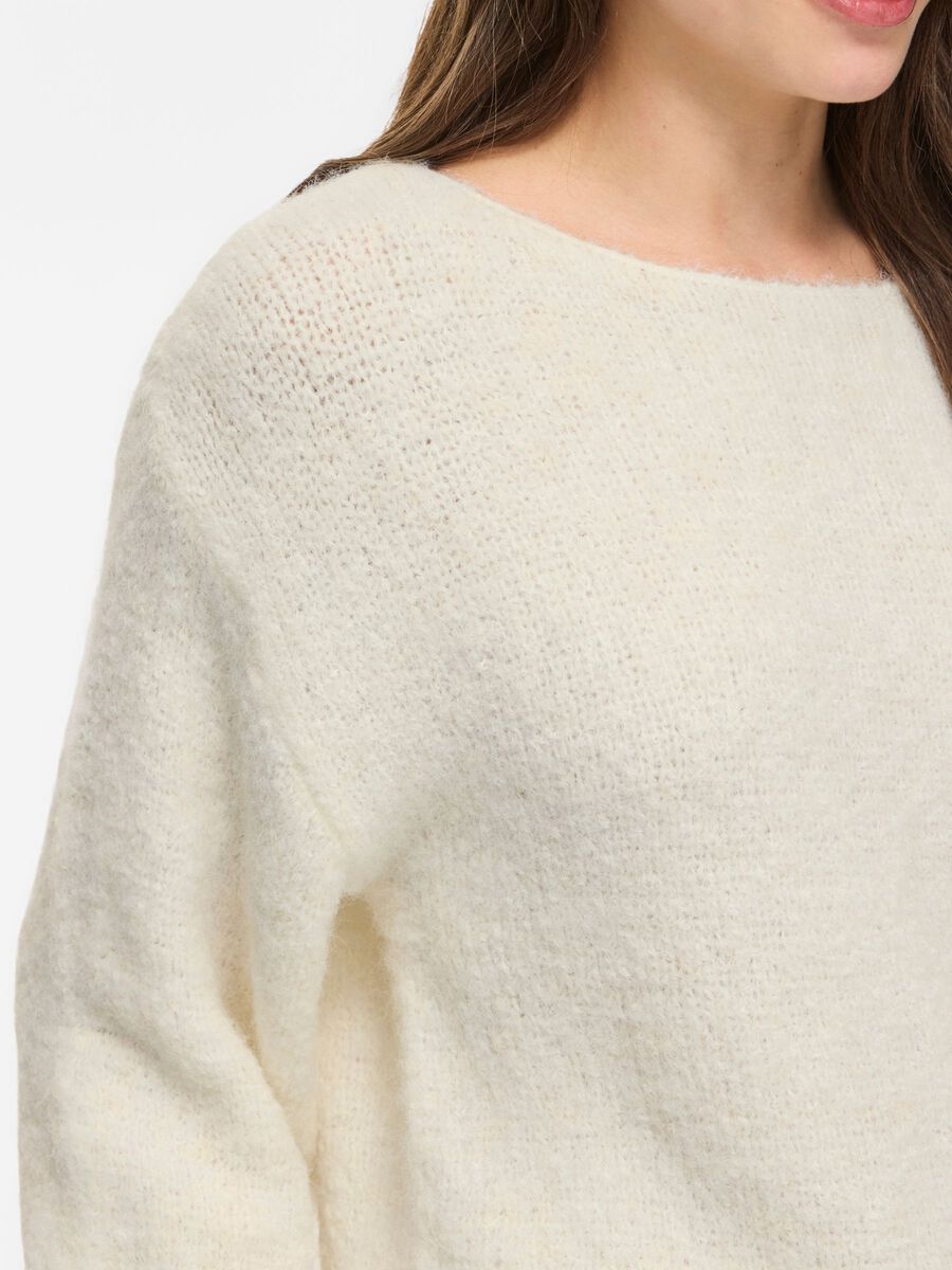 En kvinde viser en VILA 155323 Vimarley offwhite-sweater frem, hvor man ser fra skuldrene til midten af overkroppen, og hun står let drejet mod højre.