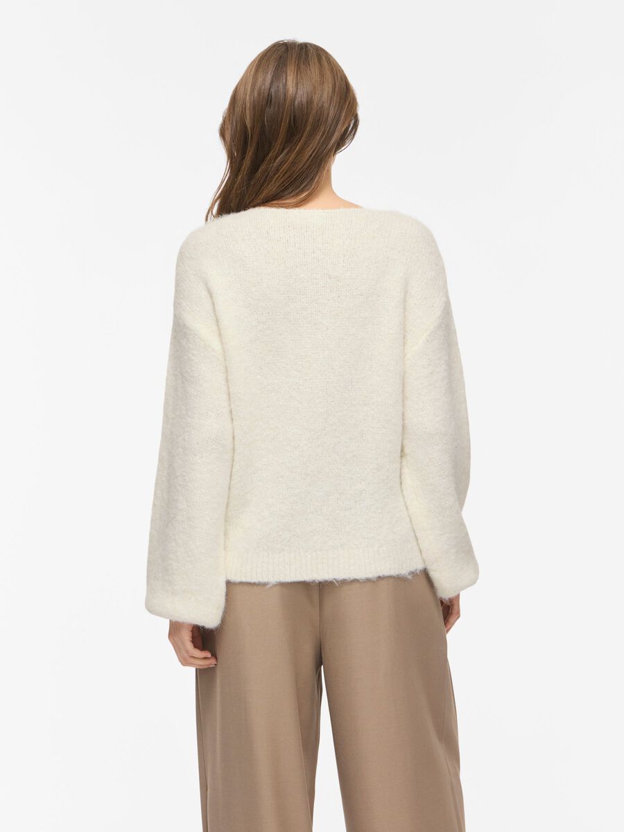 Kvinde set bagfra iført en offwhite sweater fra VILA Vimarley og beige bukser på en hvid baggrund.