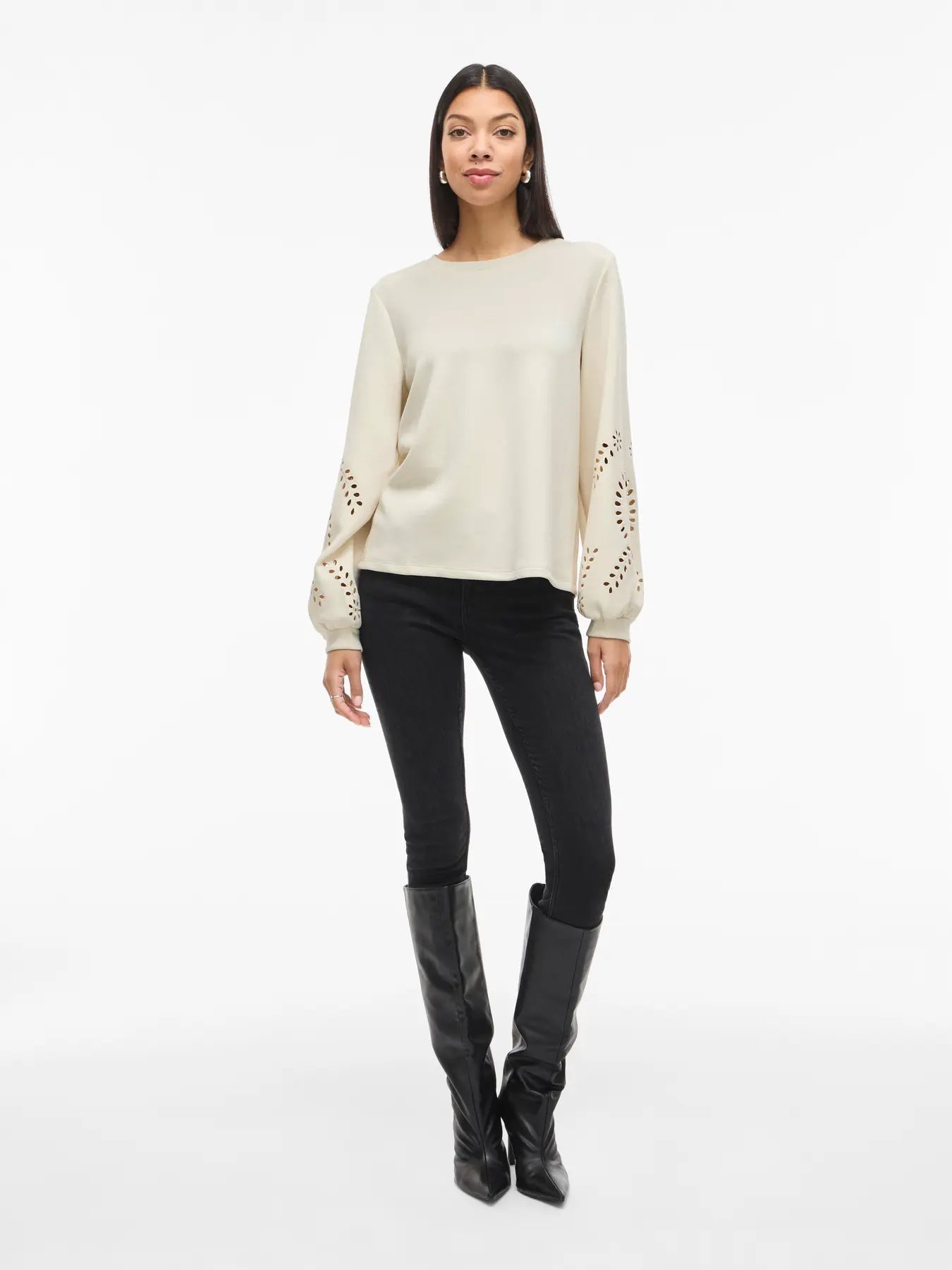 Kvinde i VILA Visandy: Offwhite sweatshirt, sorte bukser og høje sorte støvler på en hvid baggrund.