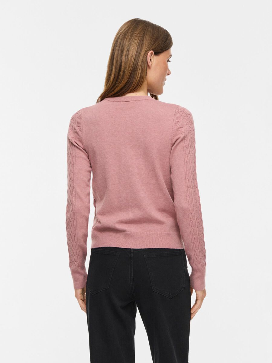 Kvinde med lysebrunt hår iført en VILA Vikerry Gammelrosa-cardigan, der står med ryggen til i sorte jeans og en lyserød trøje.