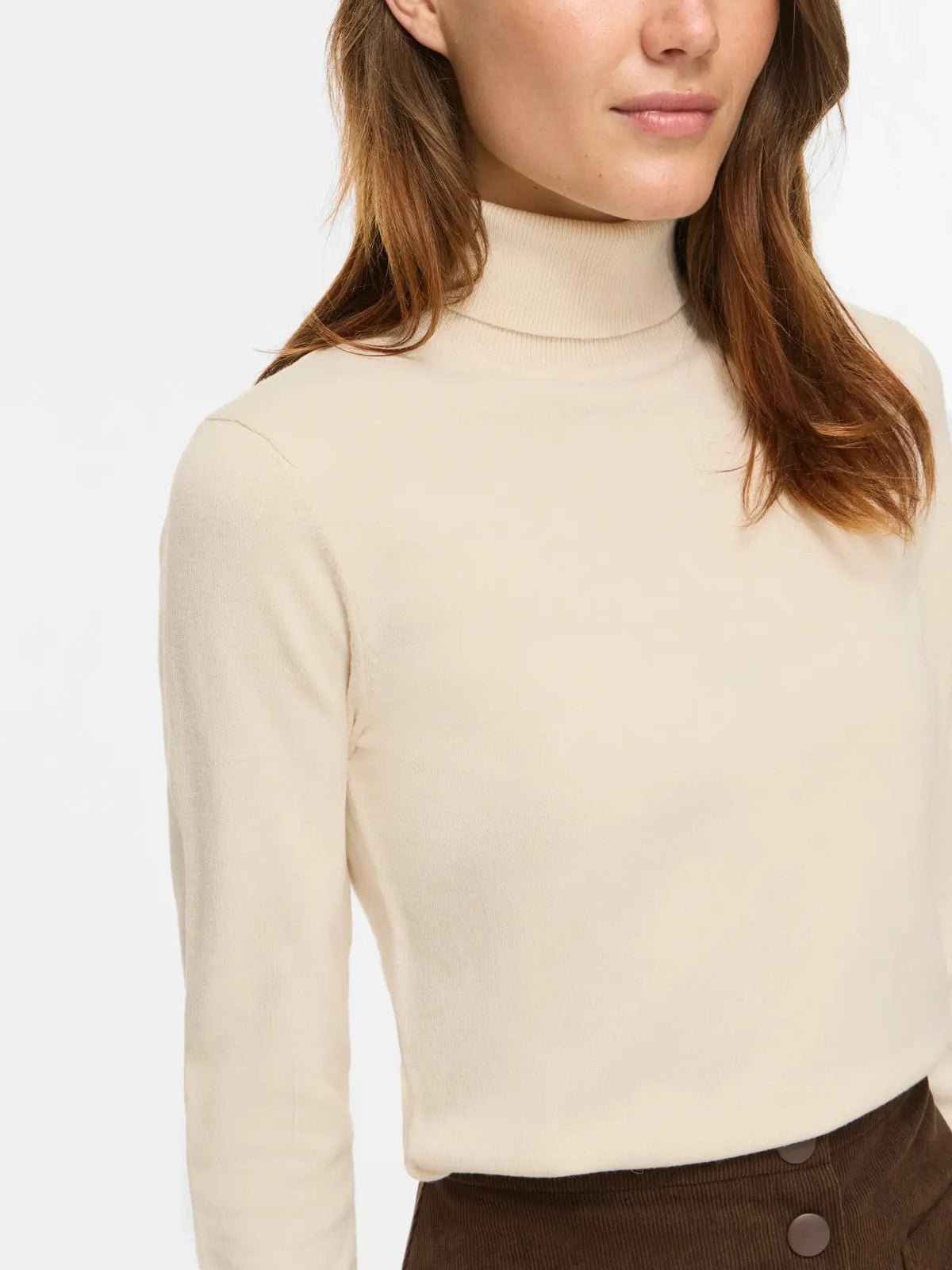 En person har VILA Malu Off White-top på sammen med brune bukser og ses fra skuldrene til taljen på en ensfarvet baggrund.