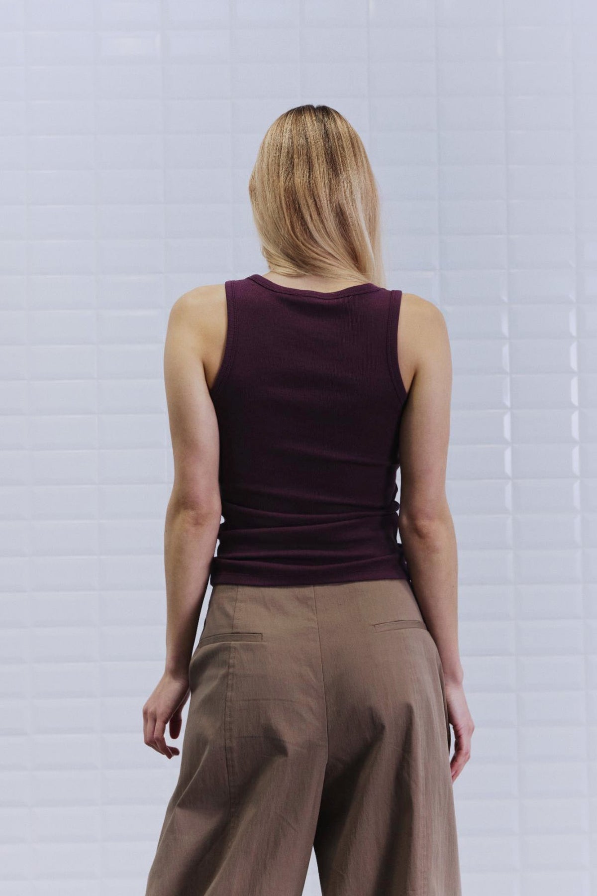 En person med langt blondt hår iført en tætsiddende WithBlack Dordi Bordeaux-dametop og beige bukser, set med ryggen til kameraet.