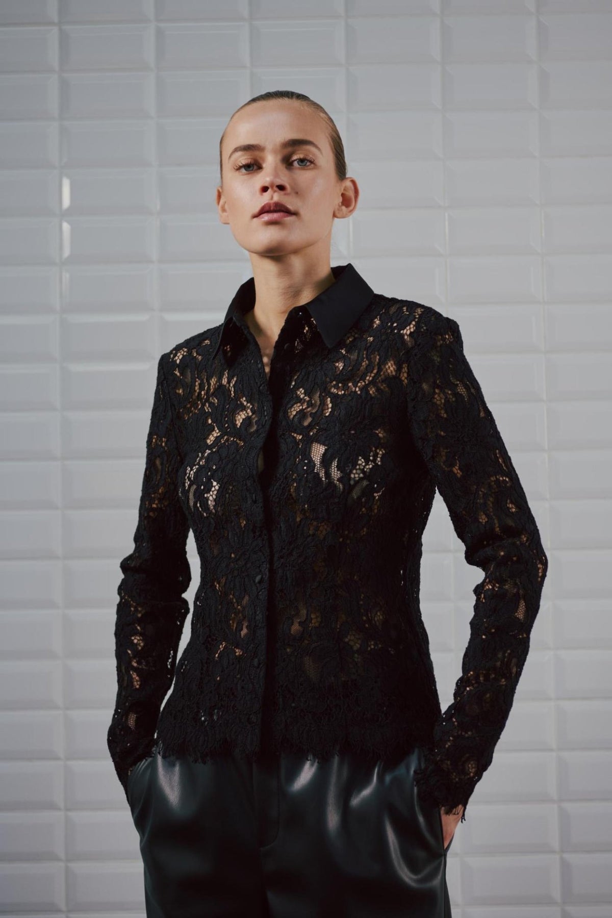 Person iført en sort, langærmet bluse i blonder med knapper, model 156399 | WithBlack – Jess Sort-bluse med tætsiddende halsudskæring.
