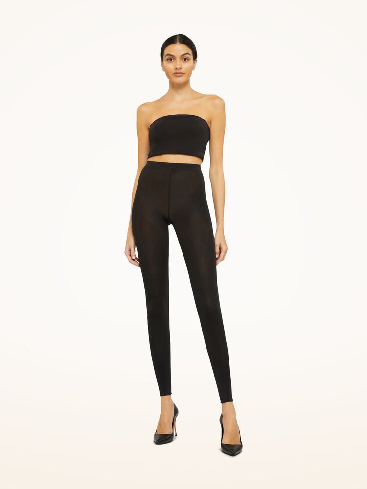 Kvinde i sort stropløs top, Wolford – Velvet 66 Black W-leggings fra Wolford og sorte højhælede sko på hvid baggrund.