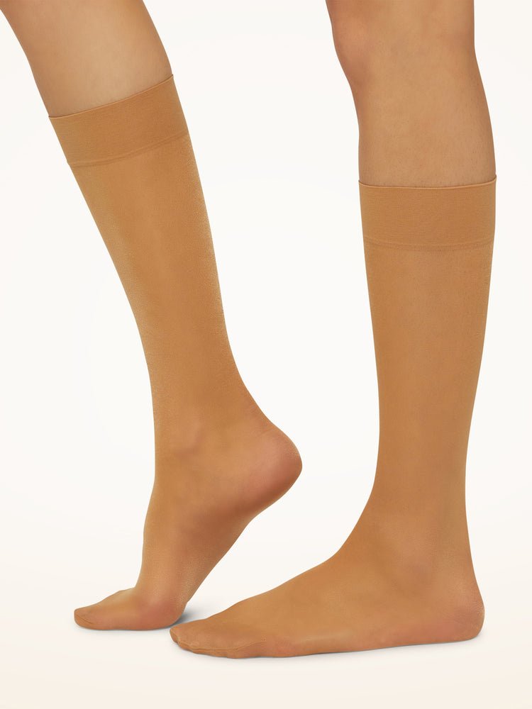 Ben i gennemsigtige, hudfarvede Wolford Satin Touch 20 Gobi 144769 på en ensfarvet, lys baggrund.