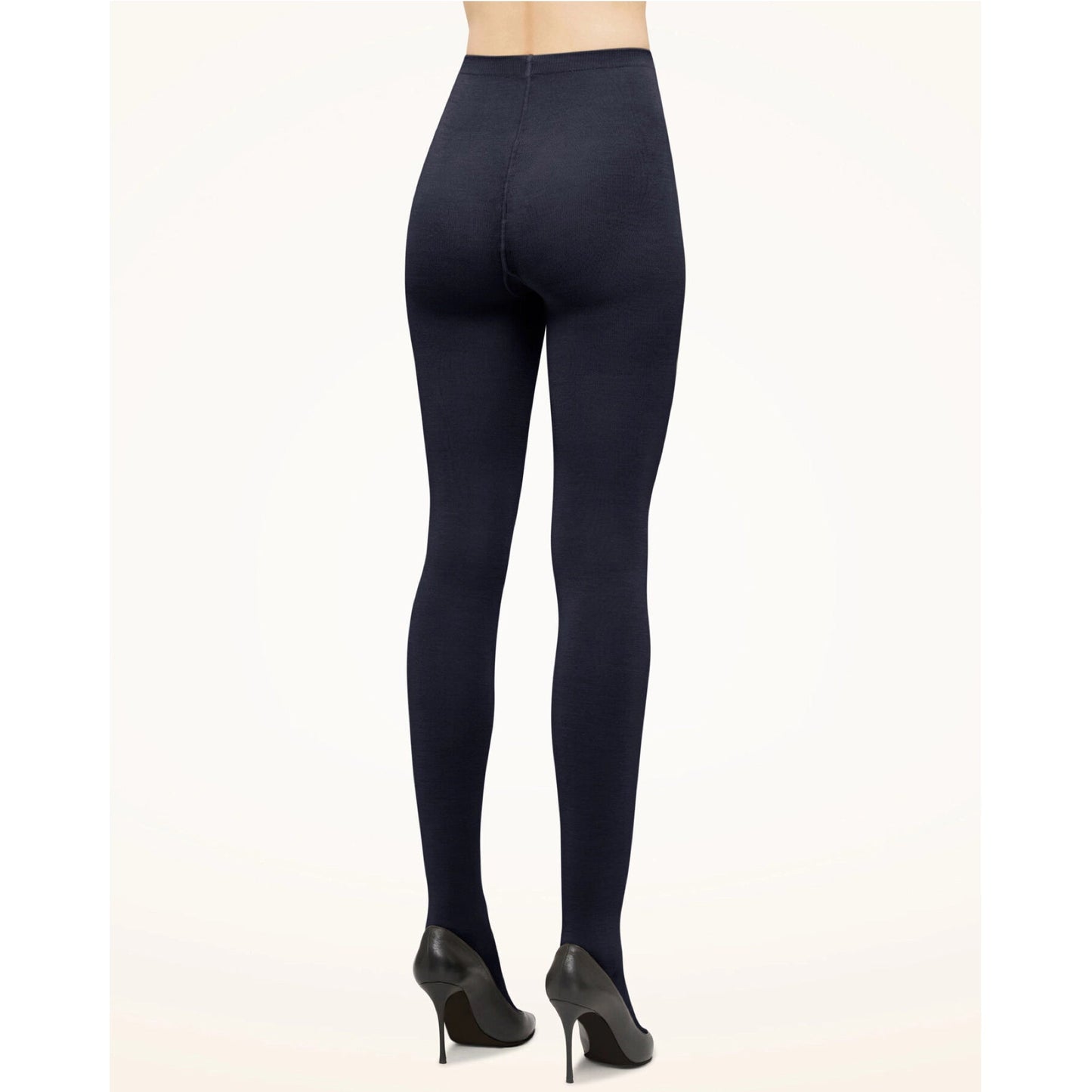 En person iført Wolford 150107 Merino Mørkeblå strømpebukser og sorte højhælede sko, set bagfra mod en ensfarvet baggrund.
