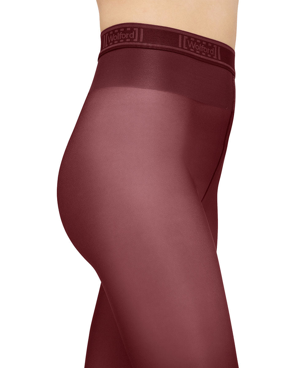 Person iført Wolford Neon 40 Bordeaux-strømpebukser med skinnende overflade og høj linning med logo, set fra siden.