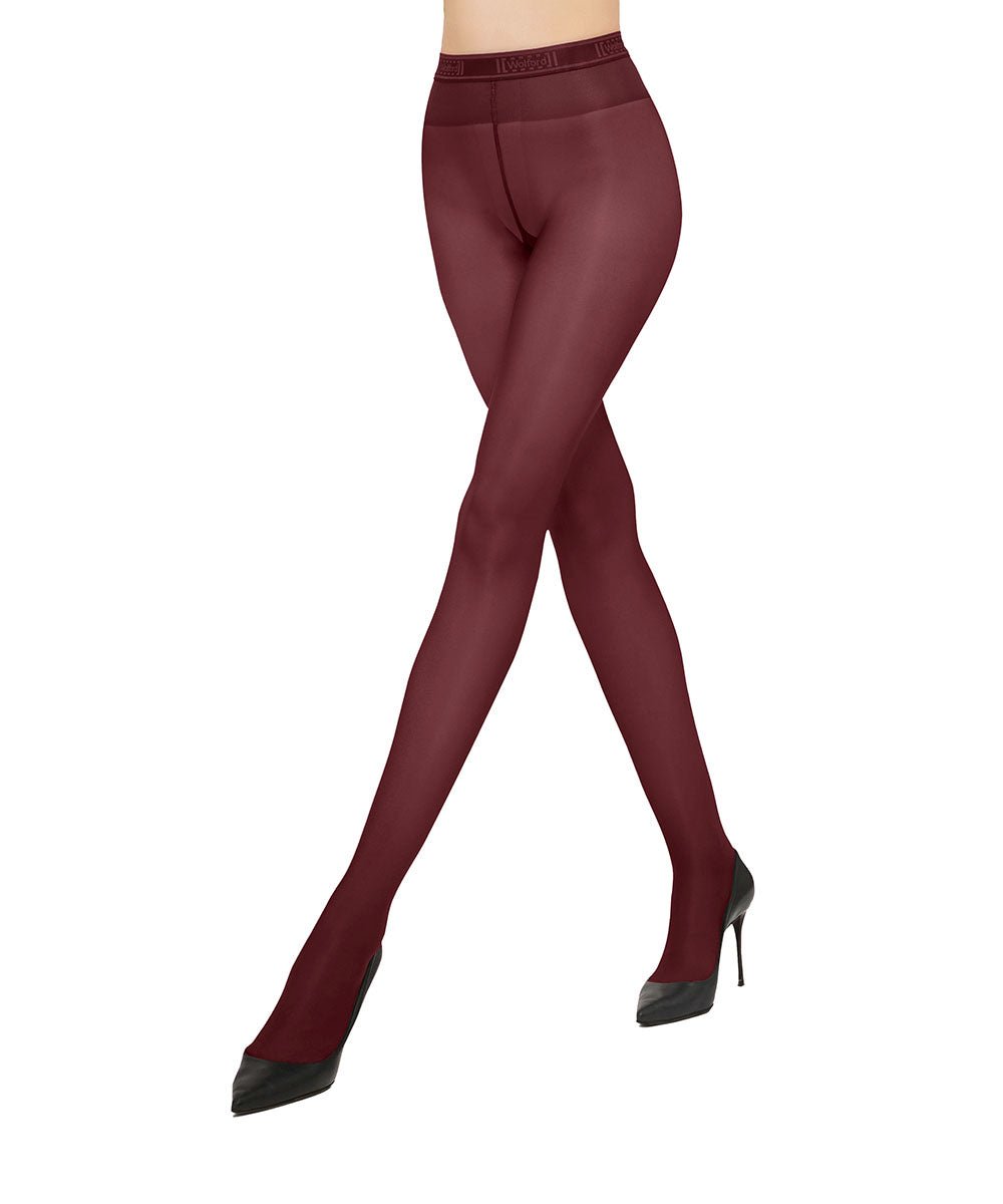 En person iført Wolford - Neon 40 Bordeaux-strømpebukser og sorte højhælede sko, med krydsede ben, foran en hvid baggrund.