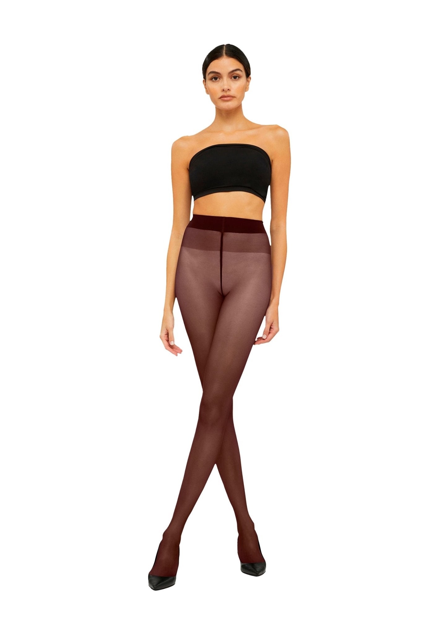 En kvinde iført en sort tube-top, Wolford Satin Touch 20-strømpebukser i farven Midnight Red og sorte højhælede sko står foran en hvid baggrund.