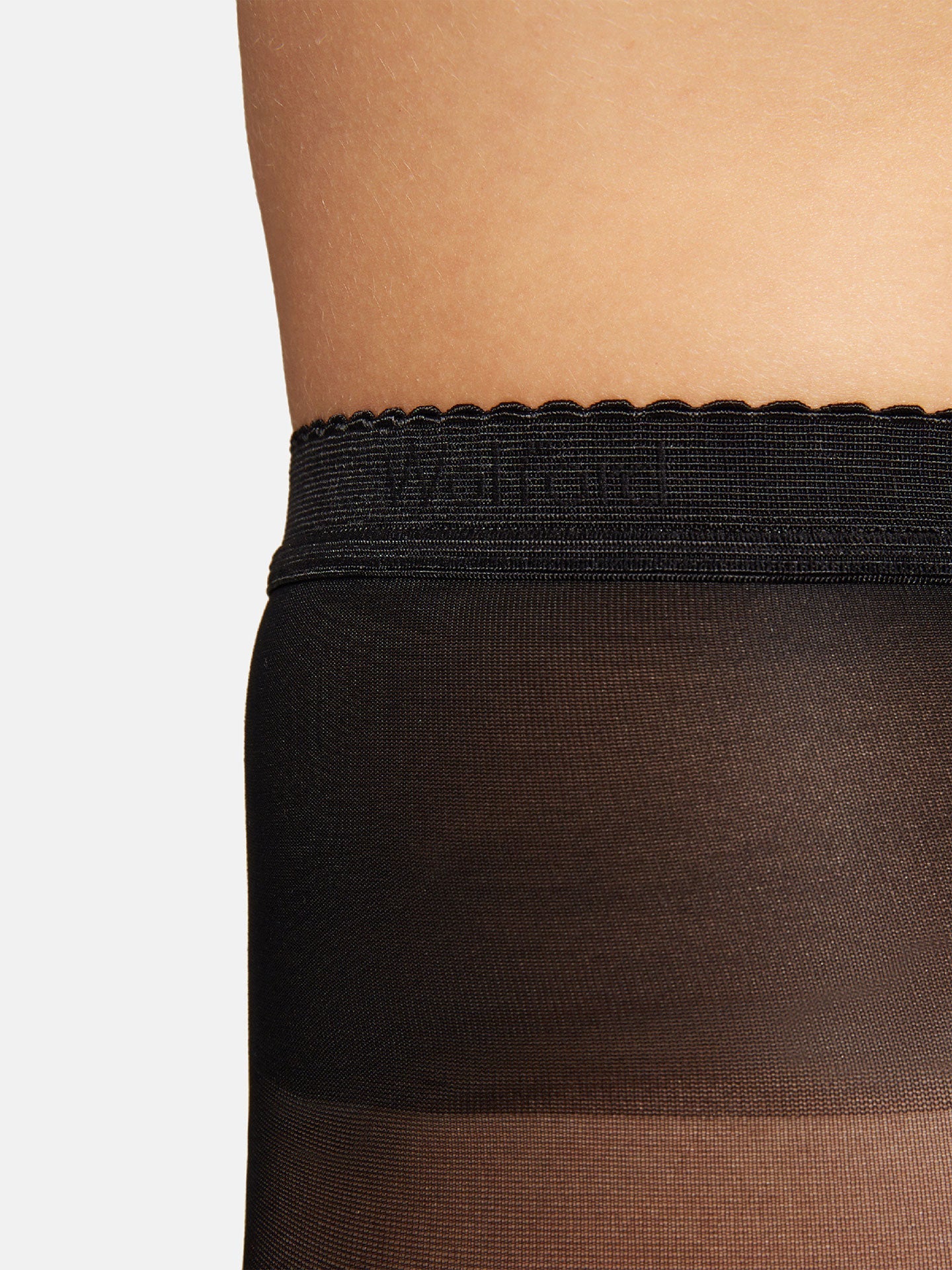 Nærbillede af det øverste lår iført Wolford Synergy 40 Black W gennemsigtige strømper med bølget elastik.